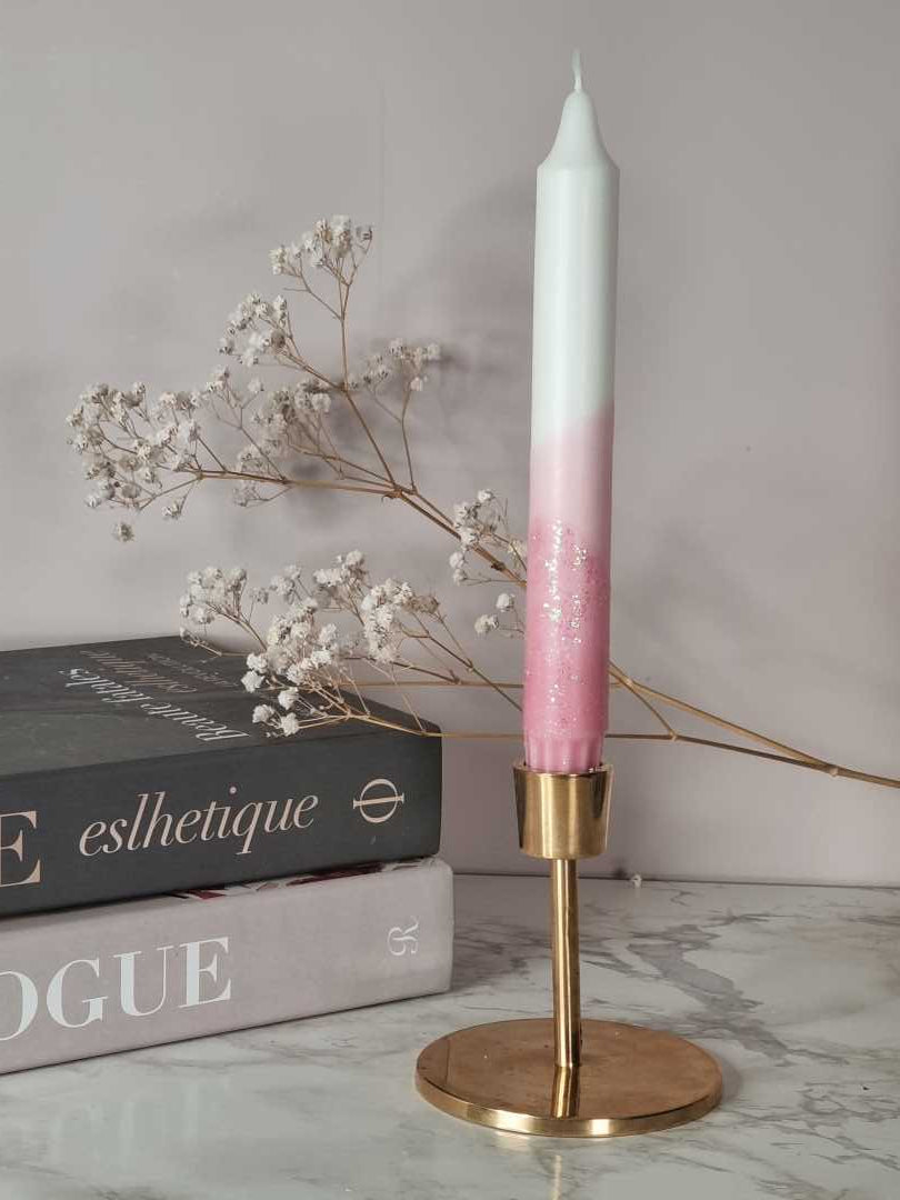 Dipdye kronelys i fargen rosa og hvitt med glitter. Lyset står i en messingstake. I bakgrunnen er det bøker og brudeslør