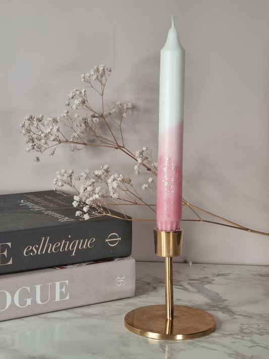 Dipdye kronelys i fargen rosa og hvitt med glitter.  Lyset står i en messingstake. I bakgrunnen er det bøker og brudeslør