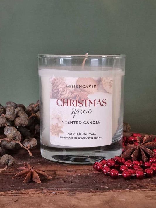 Et duftlys som står på et trefat med grønn bakgrunn. Dekoret med julepynt, og stjerneanis. Duftlyset heter Christmas spice og er fra designgaver. Lyset er laget i ren soyavoks og produsert i Skjærviken, Norge
